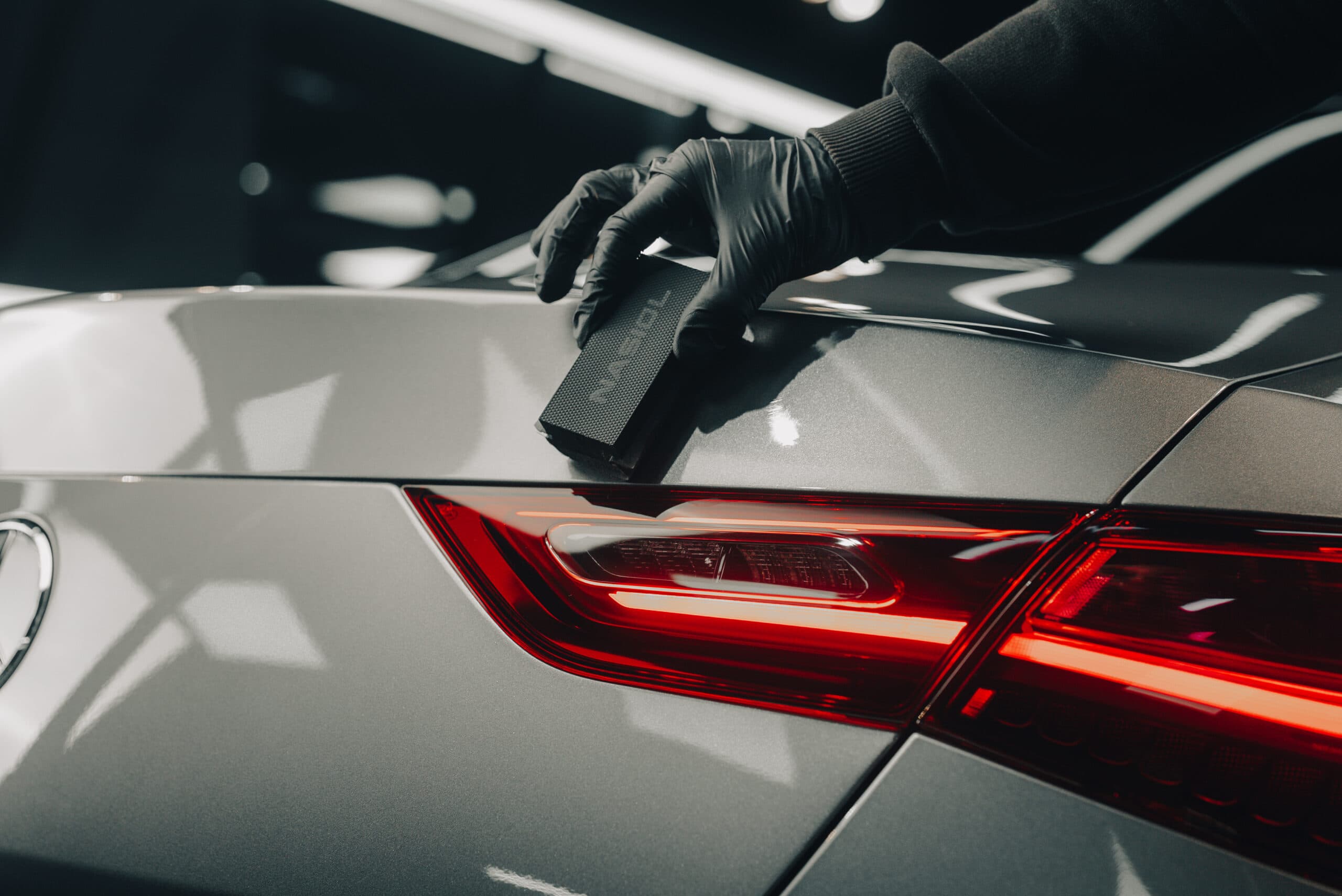 A technician applying a ceramic maintenance product to a freshly coated vehicle